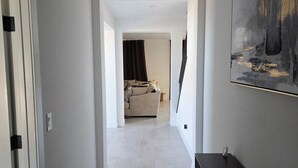 Ein Flur mit einer Tür links, einem Gemälde rechts und einem Zimmer am Ende mit einem Bett und Vorhängen.