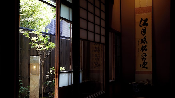 Una habitación japonesa tradicional con suelo de tatami, una puerta corrediza shoji y un rollo de caligrafía.