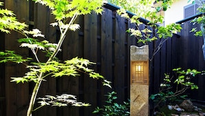 Un jardín con valla de madera, un farol de piedra y suelo cubierto de musgo.