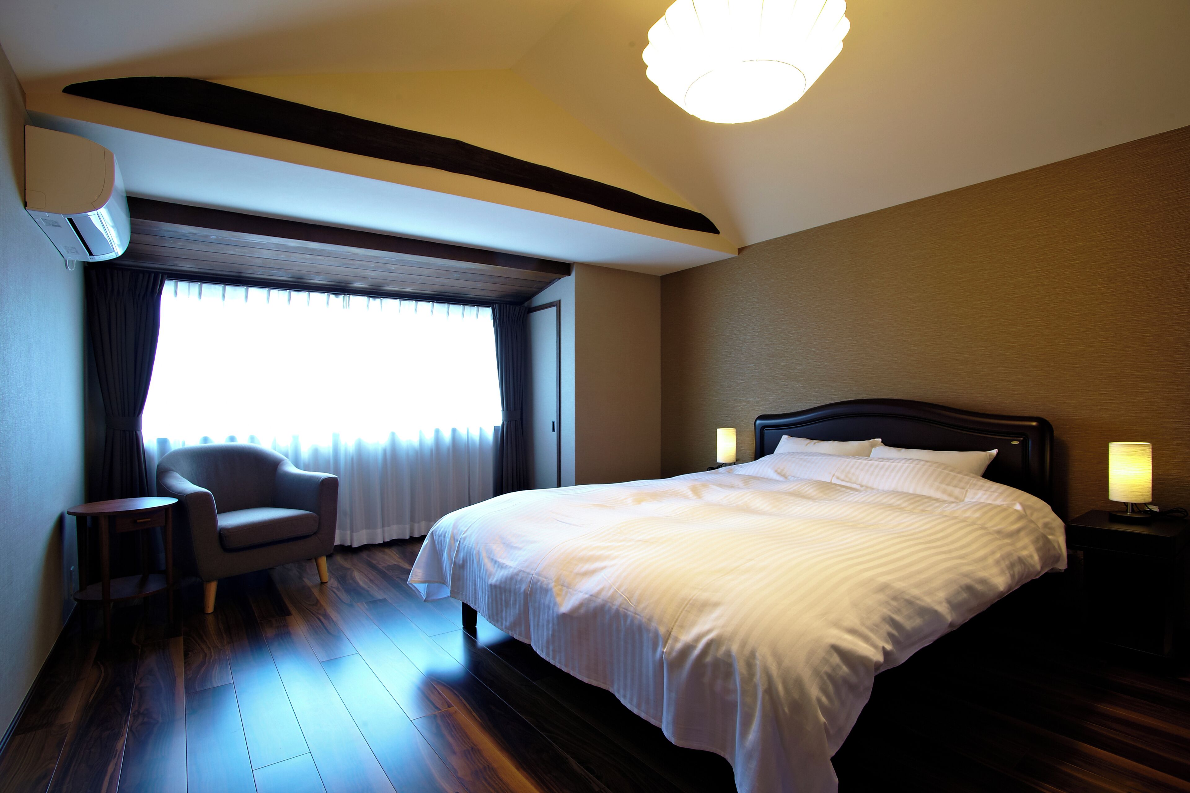 Ein Hotelzimmer mit einem Bett, Nachttischlampen, einem Sessel und einem Fenster mit Vorhängen.