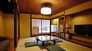 Una habitación japonesa tradicional con suelo de tatami, una mesa baja, cojines, puertas correderas y un televisor.