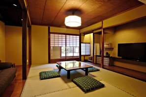 Ein traditioneller japanischer Raum mit Tatami-Boden, einem niedrigen Tisch, Kissen, Schiebetüren und einem Fernseher.