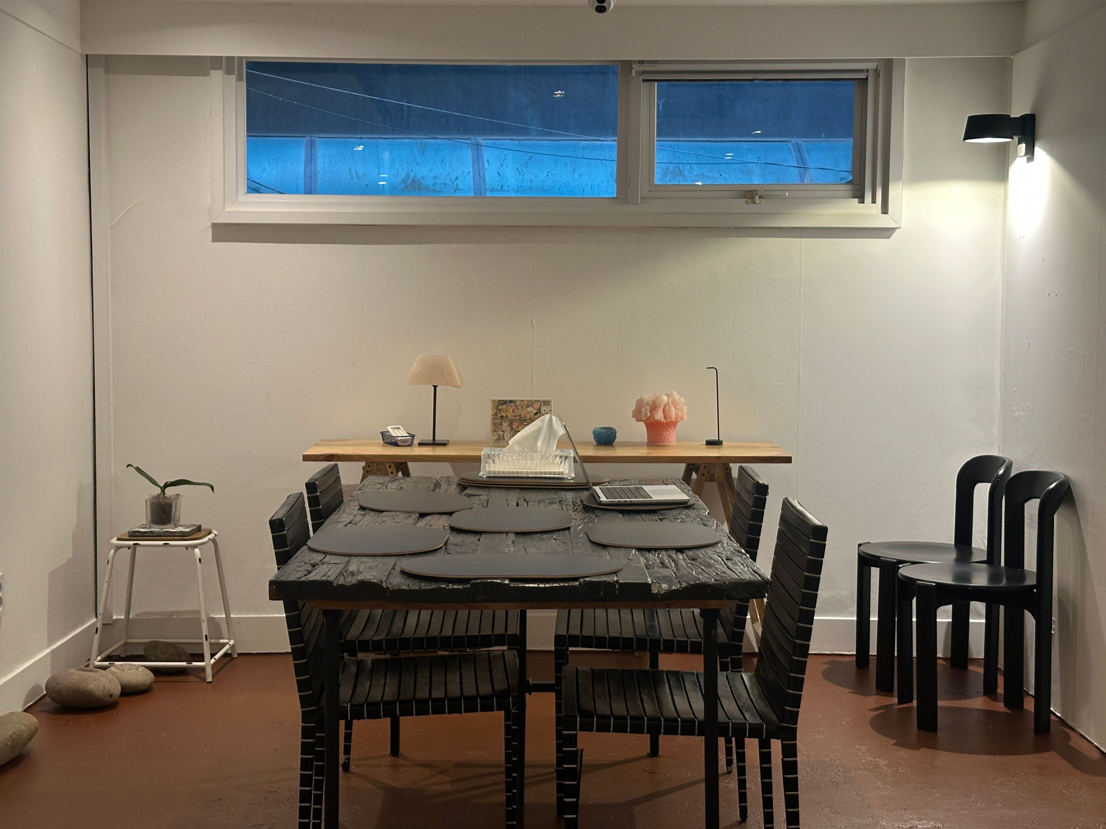 A dining area with a table, chairs, a laptop, a lamp, and a window with a view.