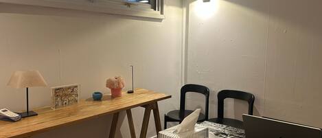 Une petite pièce avec un bureau en bois, un ordinateur portable, deux chaises, une lampe et une fenêtre.