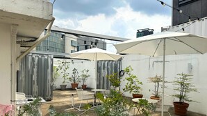 Een terras buiten met witte parasols, potplanten en tuinmeubilair.