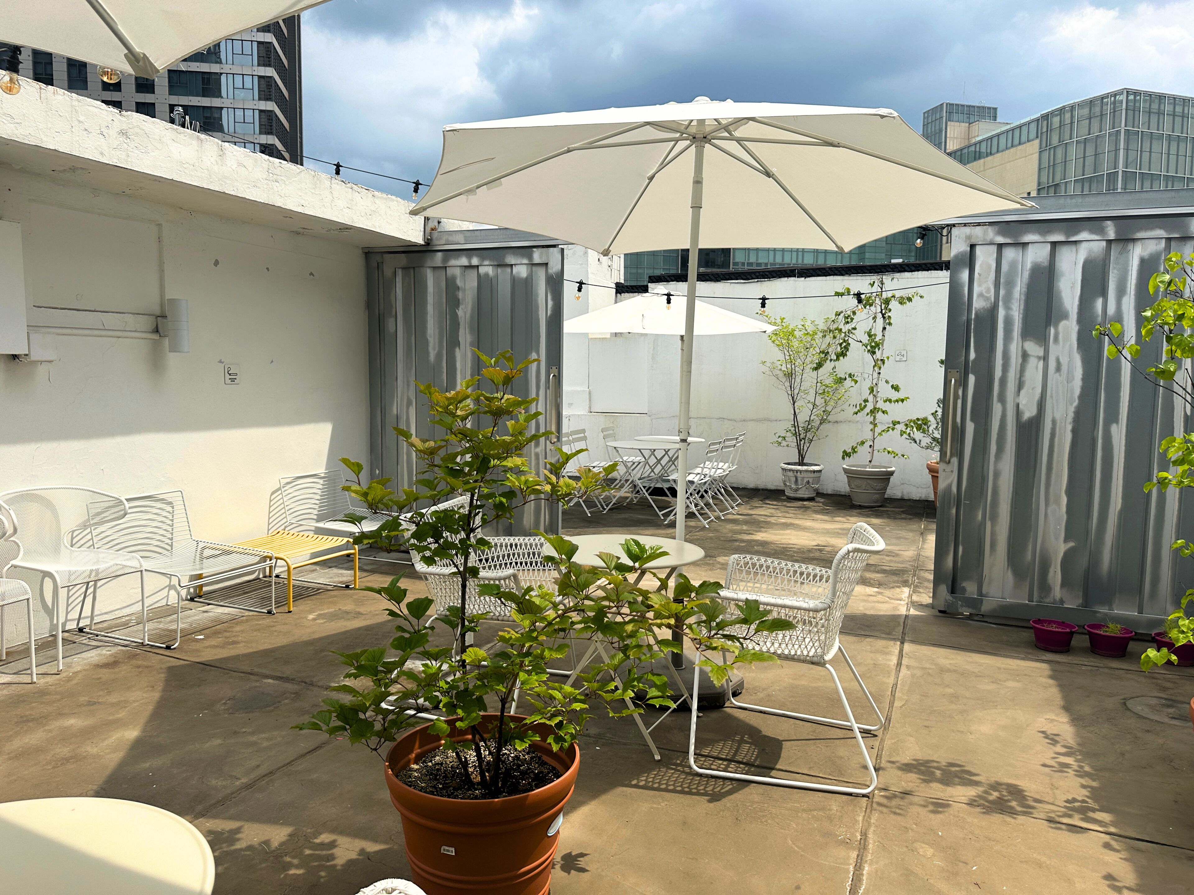A rooftop patio with outdoor seating, a large umbrella, and potted plants.