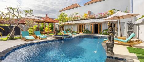 Una piscina con sillones de descanso, una pérgola y una estatua.