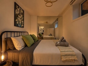 A bedroom with a bed, pillows, a bedside lamp, a towel, and a painting on the wall. - Luxury Suite on Shaganappi | Sleeps 4 | Private (Calgary)