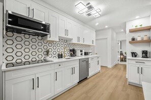 A modern kitchen with white cabinets, a microwave, a dishwasher, and a hexagonal tile backsplash. - Luxury Suite on Shaganappi | Sleeps 4 | Private (Calgary)