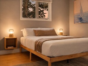 A bedroom with a wooden bed, two bedside tables with lamps, a window with a view of trees, and a painting on the wall. - 3BR bungalow near Chinook Mall, office, sleeps 8 (Calgary)