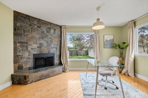 A room with a stone fireplace, a glass table with a chair, a hanging light fixture, and a view of the outdoors. - 3BR bungalow near Chinook Mall, office, sleeps 8 (Calgary)