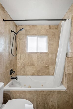 A bathroom with a bathtub, a window, and a shower curtain rod. - 3BR bungalow near Chinook Mall, office, sleeps 8 (Calgary)