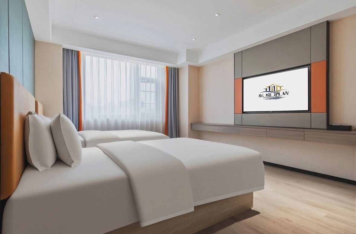A modern hotel room with a large bed, a TV mounted on the wall, and a window with curtains.