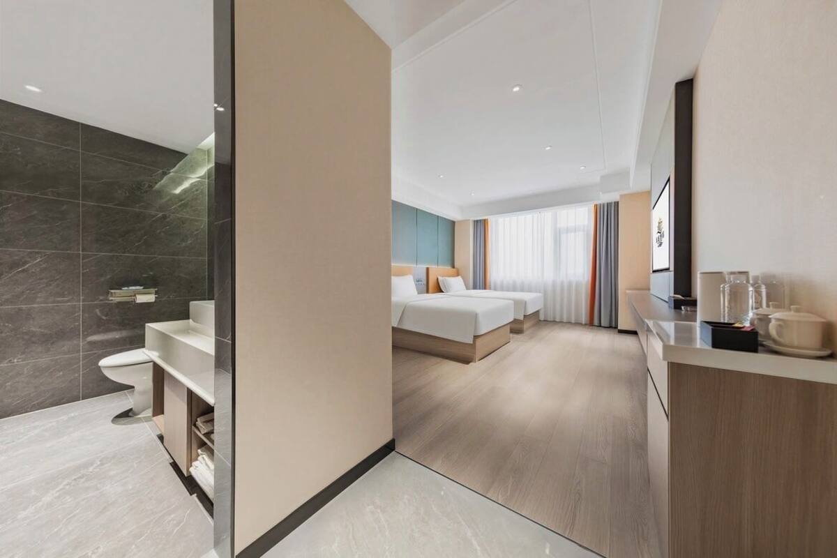 Ein modernes Hotelzimmer mit Bad, einem Bett, einem Nachttisch und einem großen Fenster.