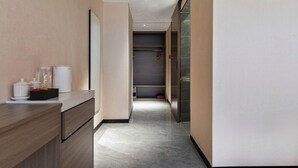 A modern hotel hallway with a wooden counter, a mirror, and a door leading to a room.