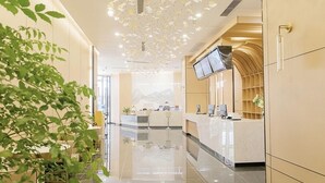 A modern hotel lobby with a reception desk, seating area, and a large TV screen.
