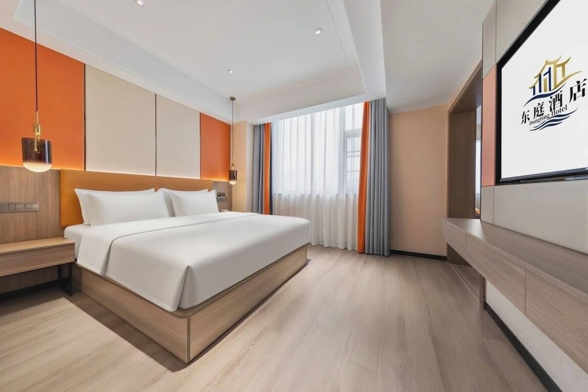 Ein modernes Hotelzimmer mit Bett, Nachttisch und einem großen Fenster mit Vorhängen.