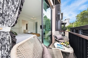 A balcony with wicker furniture, a glass door leading to a bedroom, and a table with a magazine and glasses.