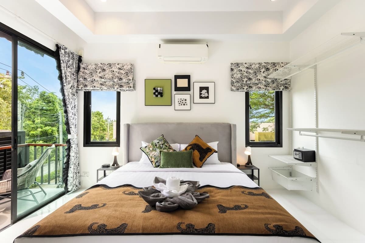 Un dormitorio con una cama, dos mesitas de noche, una ventana con cortinas, un balcón y una estantería en la pared.