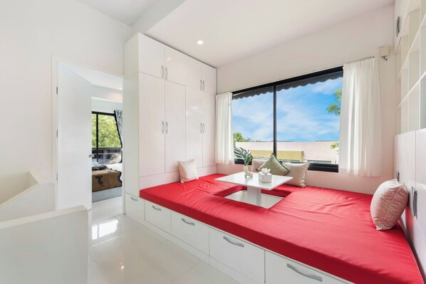 A modern bedroom with a red bed, white cabinets, and a large window with a view.