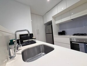 A modern kitchen with a stainless steel sink, white cabinets, a built-in oven, and a coffee machine. - Ground-Floor Comfort Peaceful 1-Bedroom Apartment (Breakfast Point)