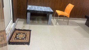 A room with a dark wooden door, a small table, an orange chair, and a patterned rug on a tiled floor. - Hotel Youvraj Inn (Ghaziabad)