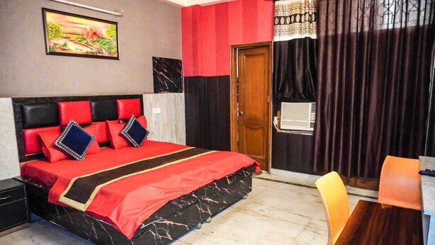 A hotel room with a bed, a desk, a chair, a door, and a painting on the wall. - Hotel Youvraj Inn (Ghaziabad)