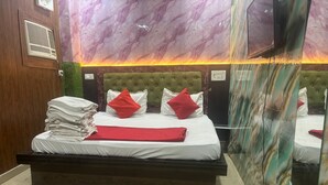 A hotel room with a marble-patterned wall, a green upholstered headboard, a bed with white bedding and red pillows, and a TV mounted on the wall. - Hotel Youvraj Inn (Ghaziabad)