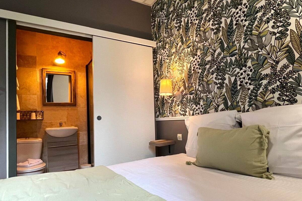 A hotel room with a bed, a bathroom with a sink and mirror, and a wall with a leafy pattern.