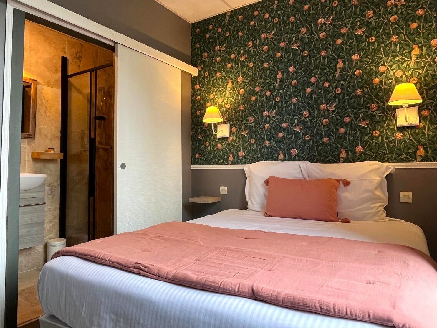 Une chambre d’hôtel avec un lit, une douche, un lavabo et un mur orné d’un motif floral.