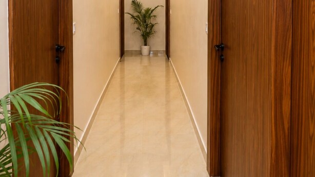 A hallway with wooden doors, a potted plant, and a tiled floor. - Ram Sadan Ayodhya (Ayodhya)