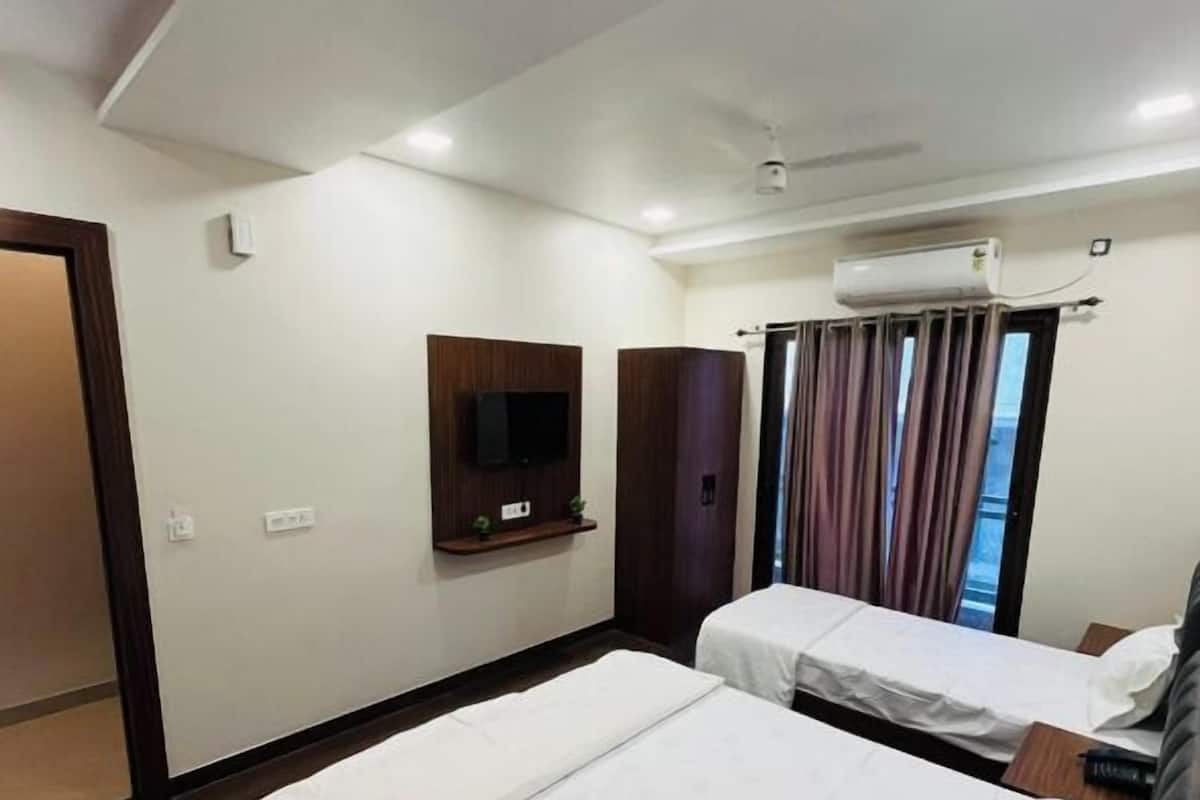 A hotel room with two beds, a TV, an air conditioning unit, and a window with curtains.