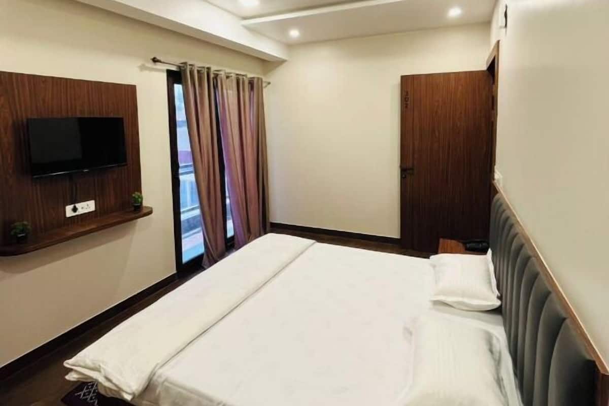 A hotel room with a bed, a TV mounted on the wall, a wooden cabinet, and a window with curtains.