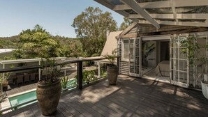Um deck de madeira com piscina, plantas em vasos e uma área de estar coberta.