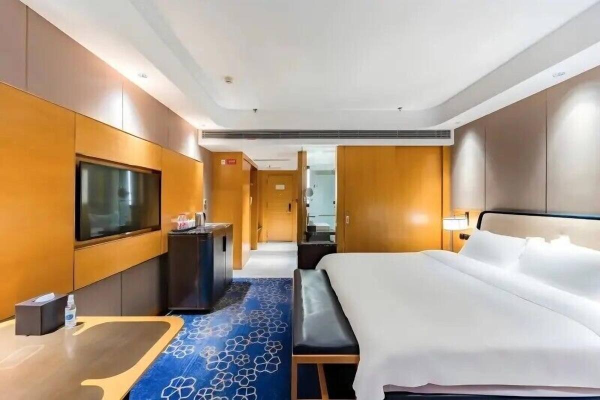A hotel room with a large bed, a television, a desk with a computer, and a bathroom visible in the background.