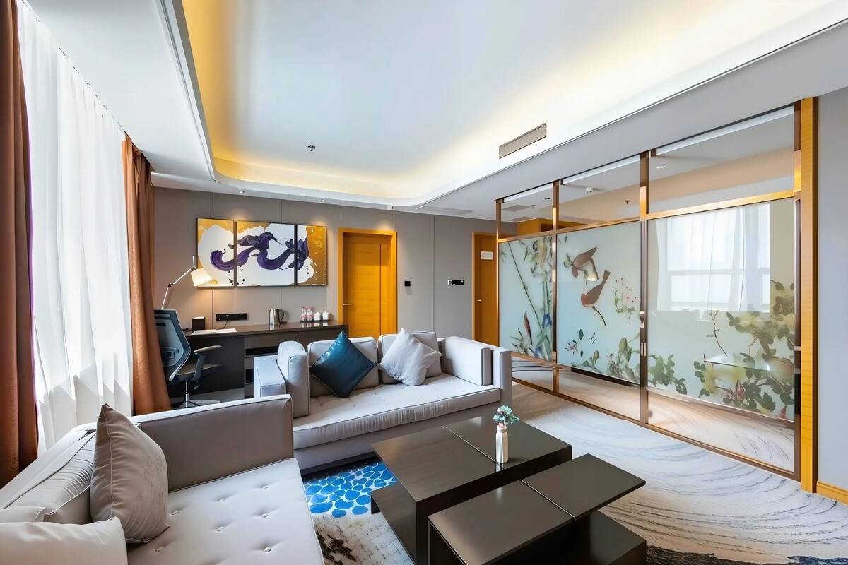 A modern hotel room with a sofa, coffee table, and a desk area.