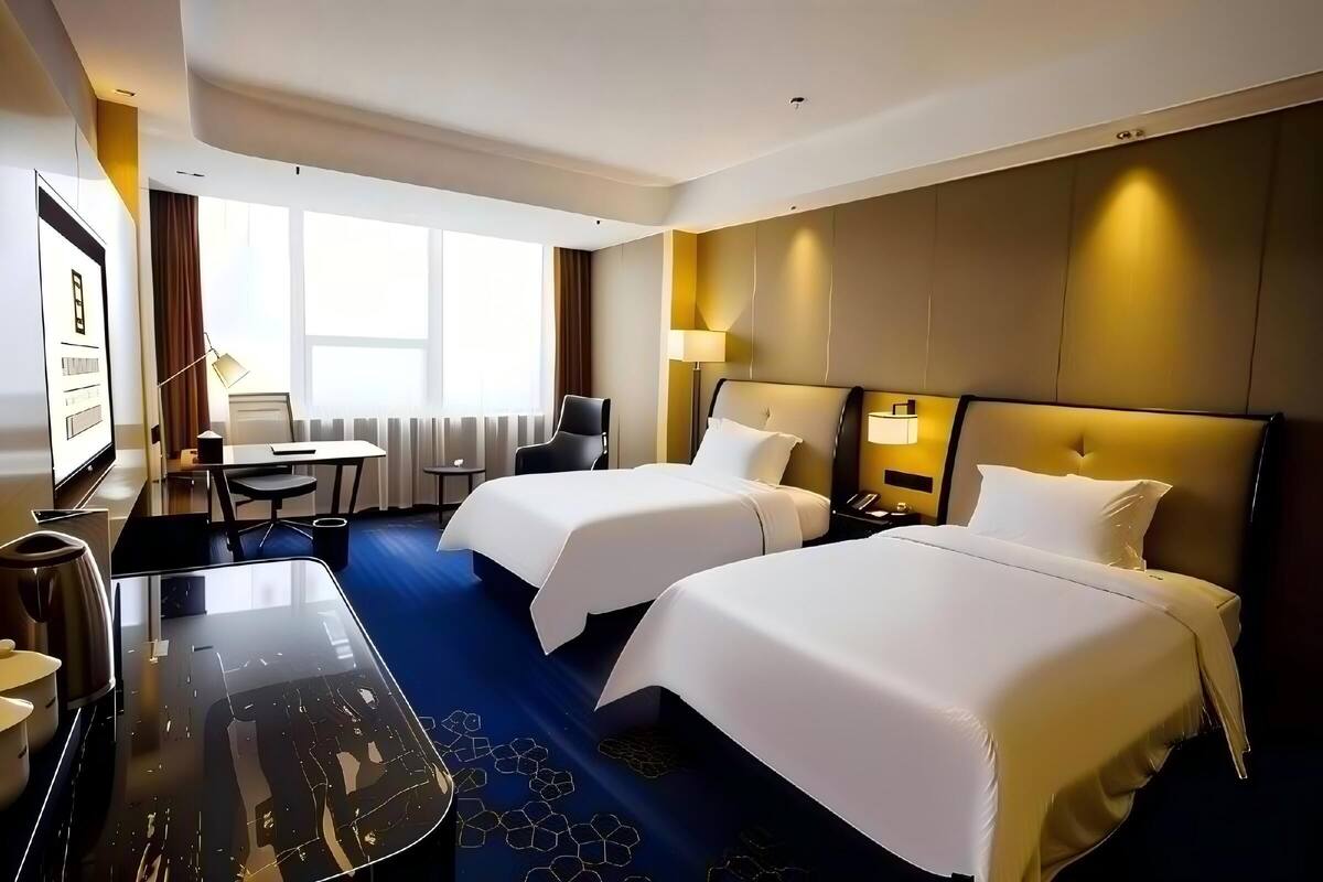 A hotel room with two beds, a desk, a chair, a TV, and a window.