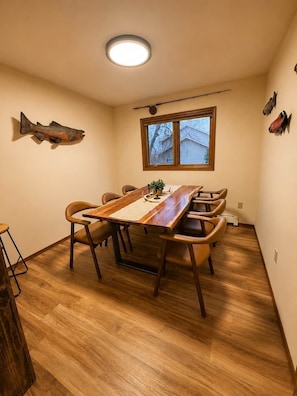 A dining area with a wooden table, chairs, a fish decoration, a window, and a ceiling light.