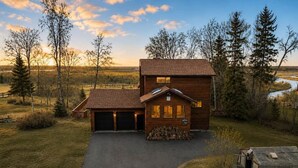Een houten chalet met twee verdiepingen en een garage, gelegen in een groene omgeving met bomen.