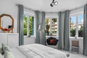 A bedroom with a bed, a desk, a chair, a lamp, a mirror, and large windows with curtains. - Luxurious 3 bedroom apartment, in the heart Cannes (Cannes)
