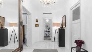 A hallway with a large ornate mirror, a chandelier, and a modern console table with a vase. - Luxurious 3 bedroom apartment, in the heart Cannes (Cannes)
