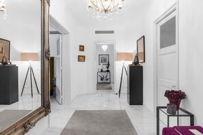 A hallway with a large ornate mirror, a chandelier, and a modern console table with a vase. - Luxurious 3 bedroom apartment, in the heart Cannes (Cannes)