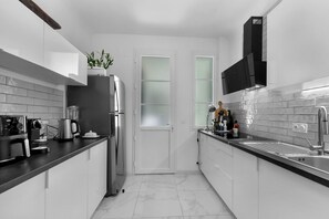 A modern kitchen with white cabinets, a stainless steel refrigerator, a coffee maker, and a plant on the counter. - Luxurious 3 bedroom apartment, in the heart Cannes (Cannes)