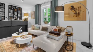 A modern living room with a white sofa, a round coffee table, a bookshelf, and a large window with curtains. - Luxurious 3 bedroom apartment, in the heart Cannes (Cannes)