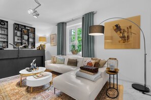 A modern living room with a white sofa, a round coffee table, a bookshelf, and a large window with curtains. - Luxurious 3 bedroom apartment, in the heart Cannes (Cannes)