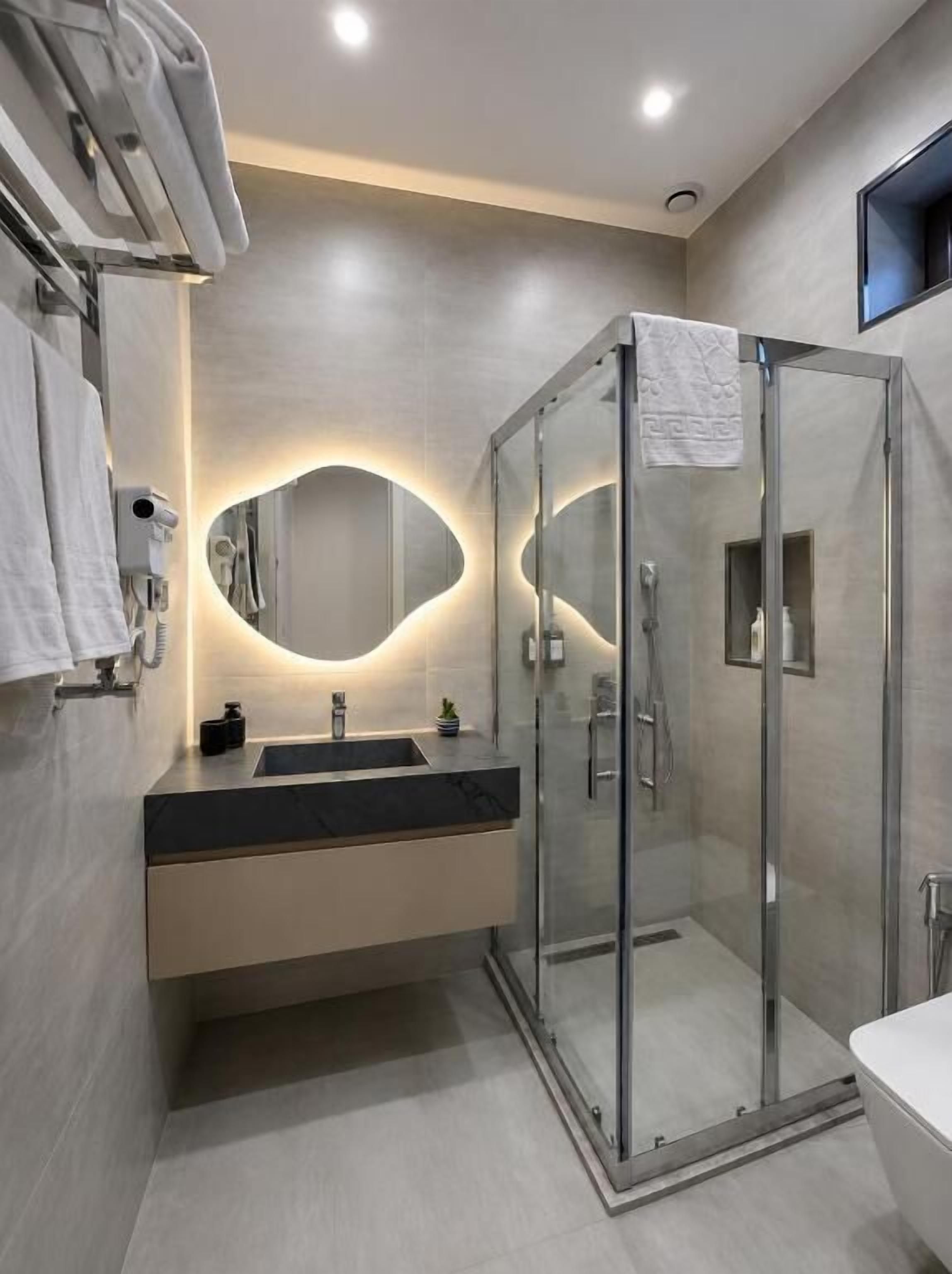 Un baño moderno con cabina de ducha de vidrio, un lavamanos con encimera negra y un espejo con un diseño de iluminación original.