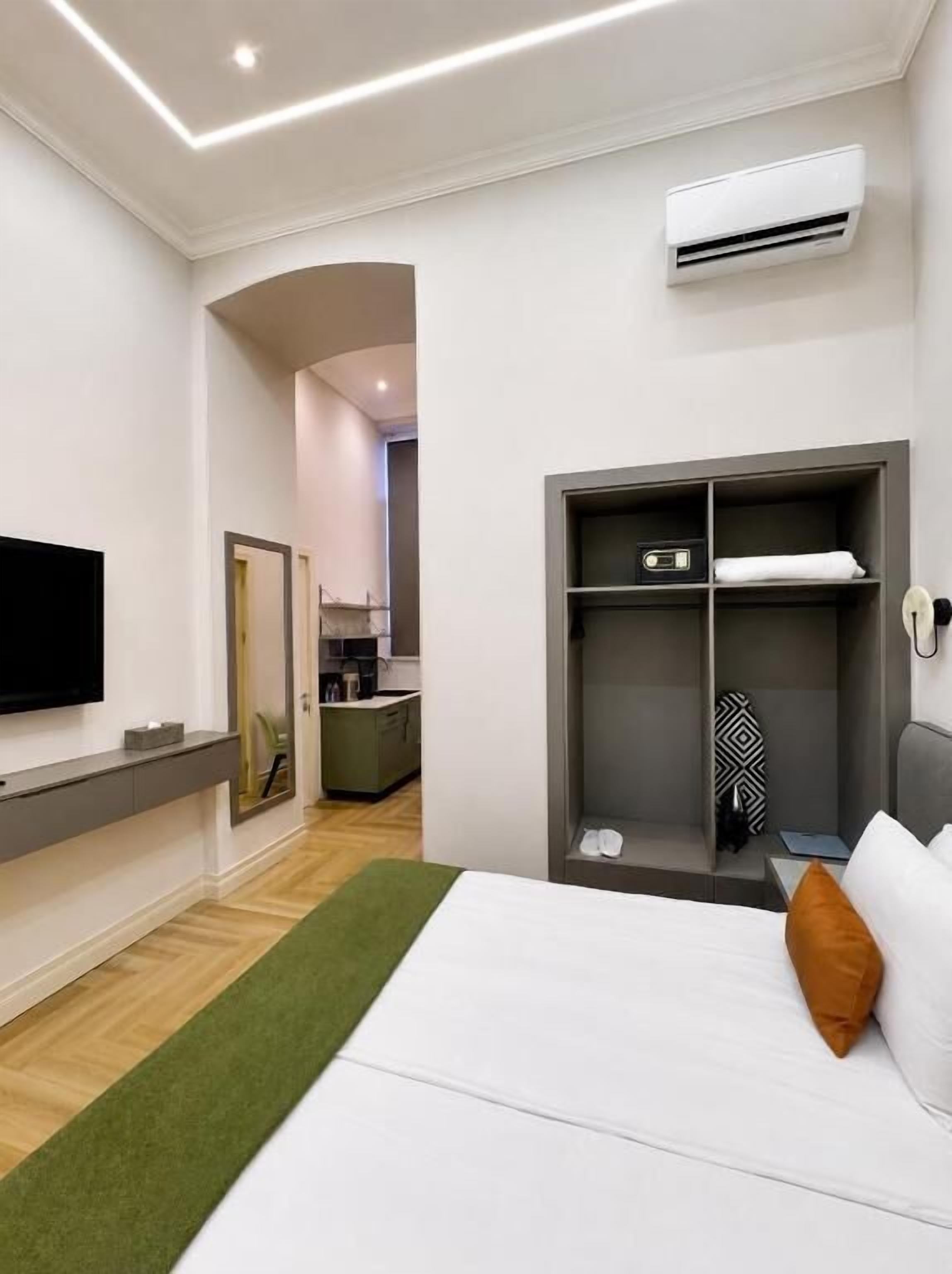 Ein modernes Hotelzimmer mit Bett, Flachbildfernseher, begehbarem Kleiderschrank und Klimaanlage.