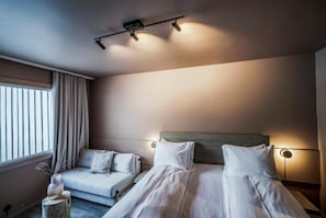A hotel room with a bed, a sofa, a nightstand, a lamp, and a window with curtains.