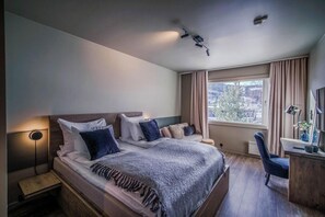 Una habitación de hotel moderna con una cama grande, mesitas de noche, un escritorio y una ventana con cortinas.