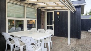 Une terrasse couverte avec une table et des chaises, une porte et une fenêtre.